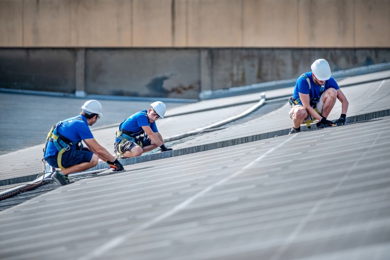 Three men working on a commercial roof performing repairs by NorCal Roofing & Gutters