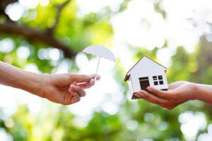A small cardboard umbrella being held by a small cardboard house by NorCal Roofing & Gutters