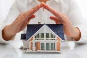 Small toy house with a person holding their hands over it by NorCal Roofing & Gutters
