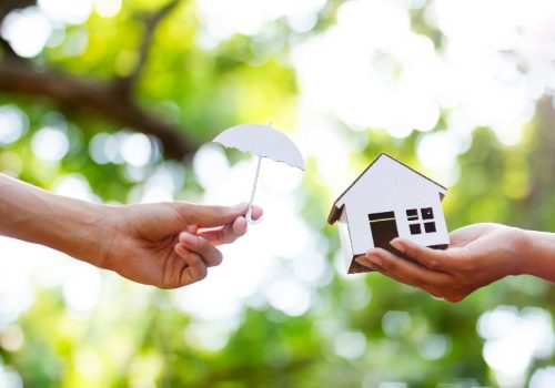 A small cardboard umbrella being held by a small cardboard house by NorCal Roofing & Gutters